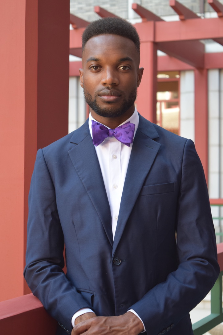 Leon Jones III wearing a navy suit and purple bow tie outdoors.